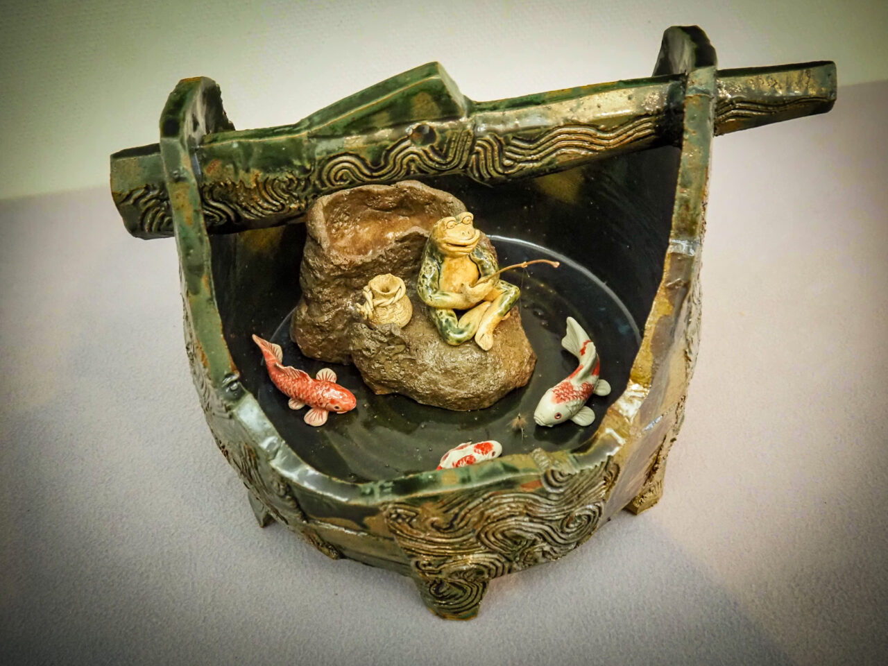 井戸の中でカエルが釣りをしているユニークな陶芸作品