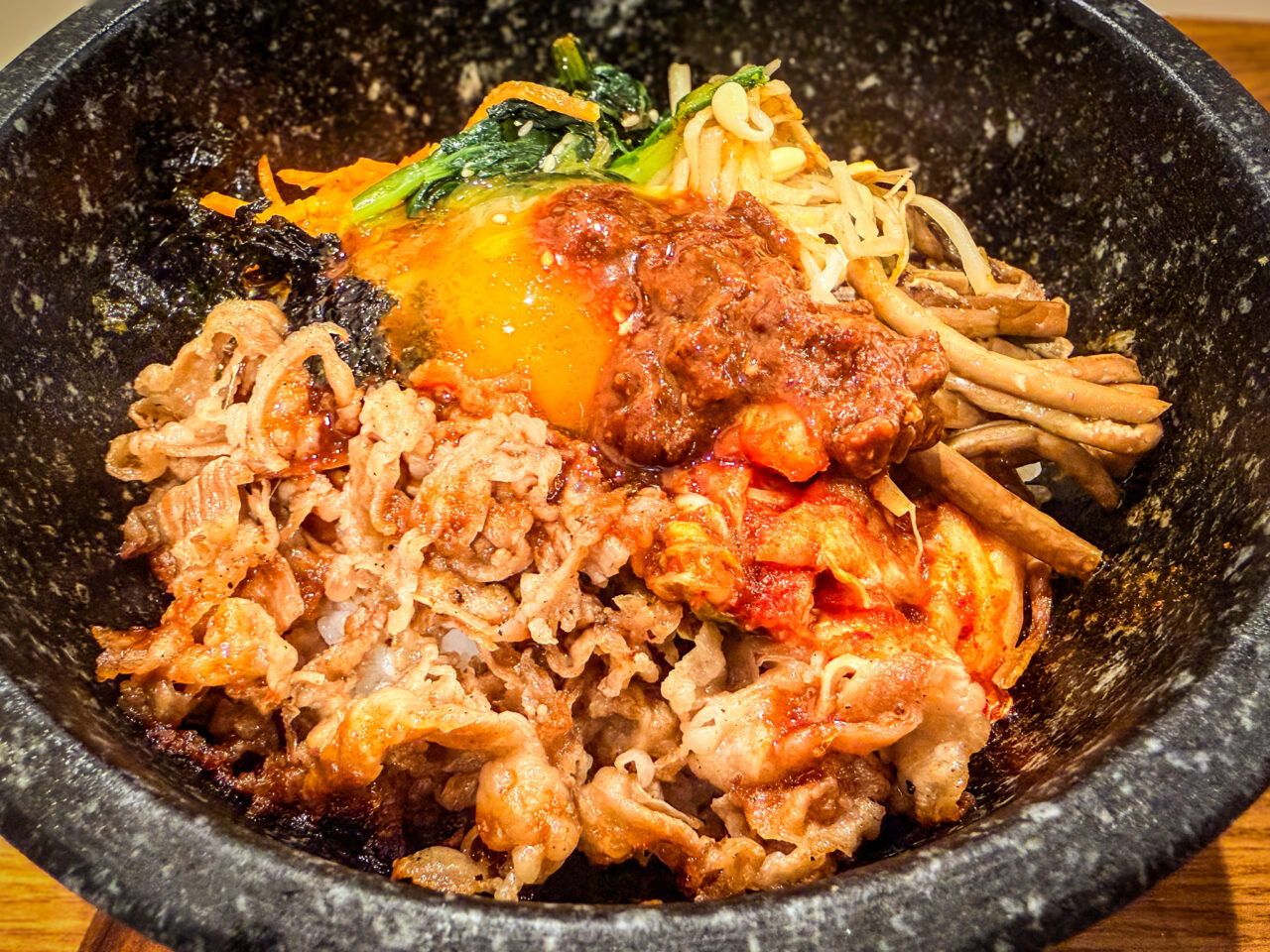 牛肉、キムチ、ナムル、卵黄が盛り付けられた石焼ビビンバのアップ