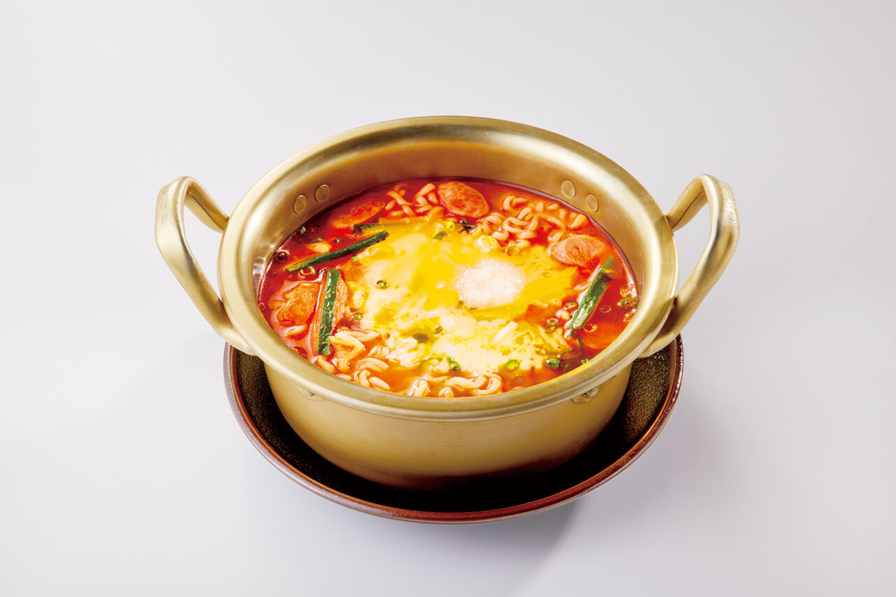 金色の韓国風手付き鍋に入った、中央にとろけるチーズとニンニクが載った旨辛ラーメン