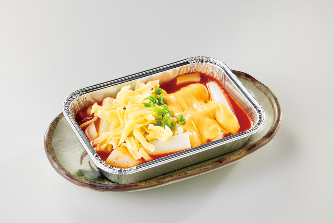 アルミホイル皿に入った、とろける2種のチーズと赤い麻辣ダレがたっぷりかかったトッポギ